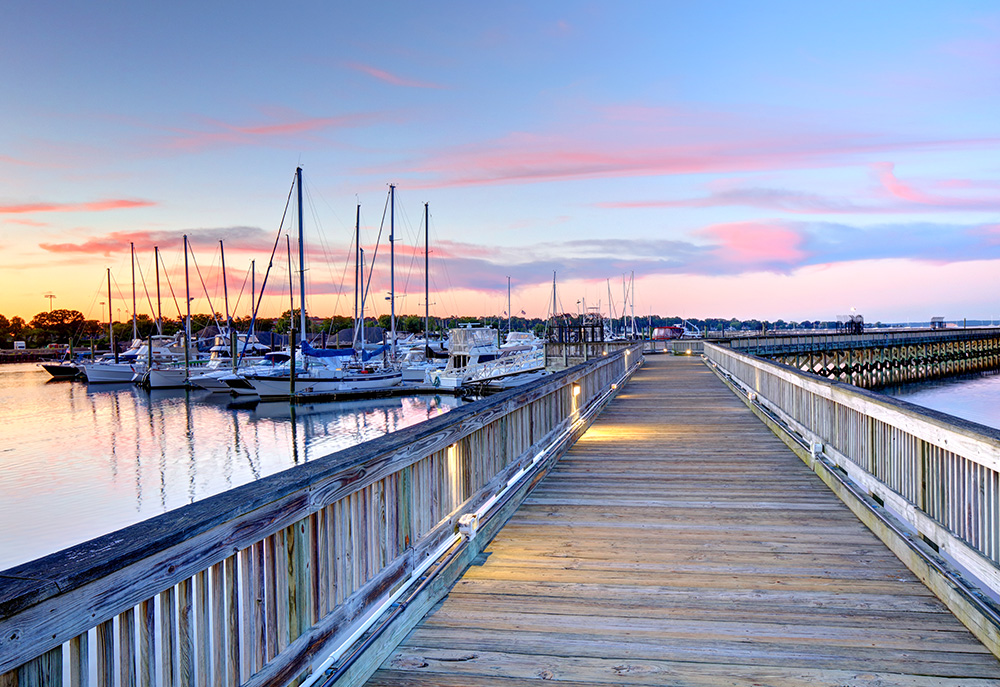 Dock with railing next to a packed marina at sunset